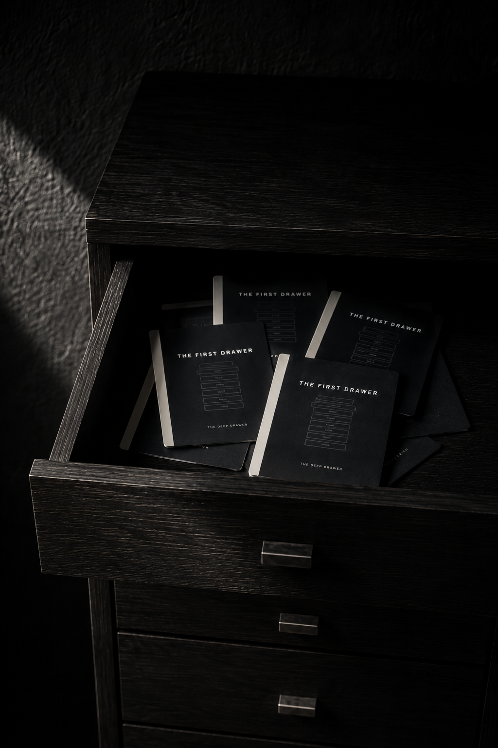 Printed THE FIRST DRAWER decks stacked inside an open drawer of a dark wooden chest